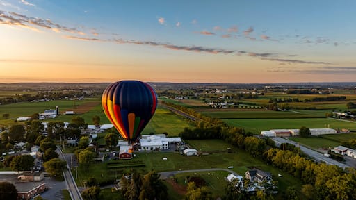 A hot air balloon over a rural landscape with fields, houses, and a road.