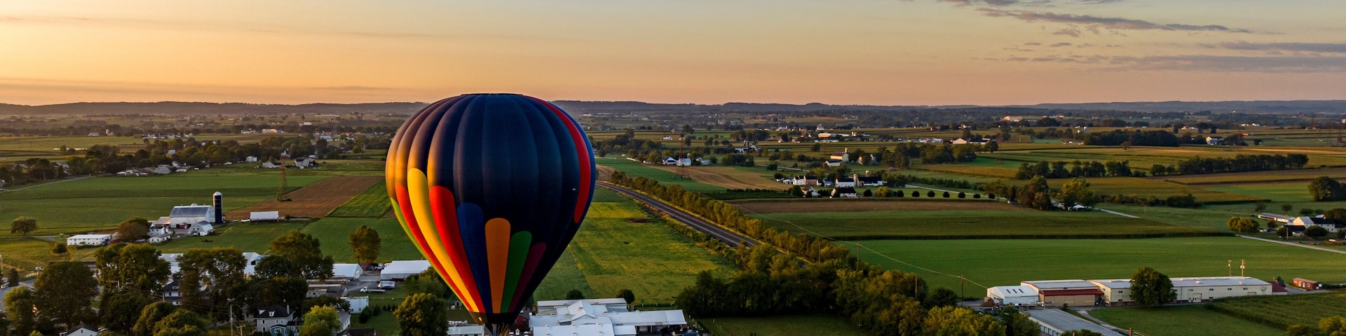 A hot air balloon over a rural landscape with fields, houses, and a road.