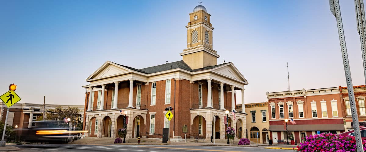 A historic building with a clock tower, pedestrian crossing signs, and a street with a metal guardrail.