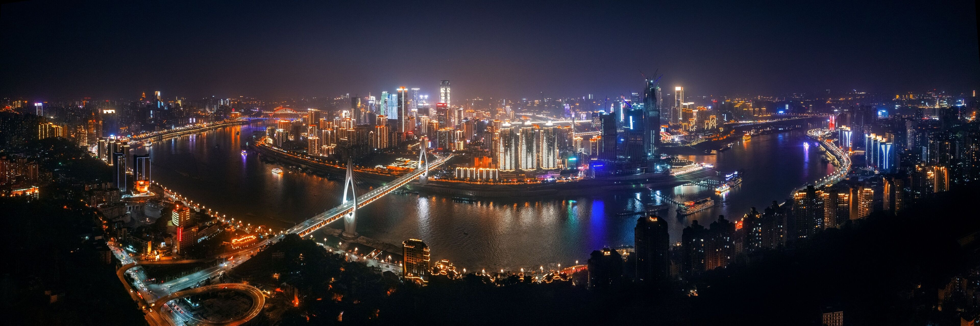 A nighttime cityscape with a prominent bridge and illuminated buildings.