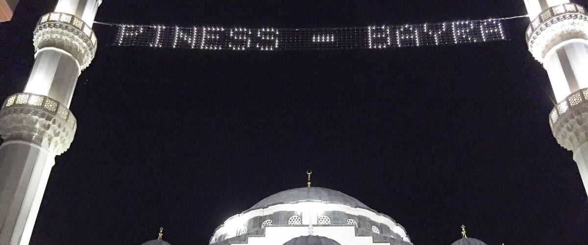 A mosque with a large illuminated sign reading "PINESS BAYRA" and a dome with Arabic calligraphy.