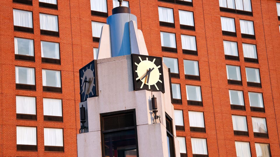 A clock tower with a modern design, set against a red brick building with multiple windows.