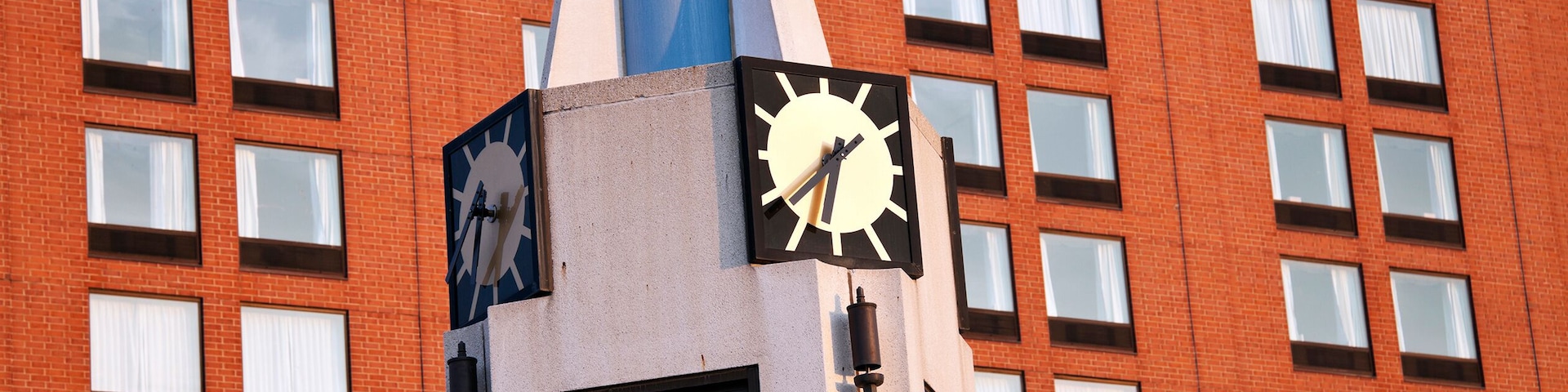 A clock tower with a modern design, set against a red brick building with multiple windows.