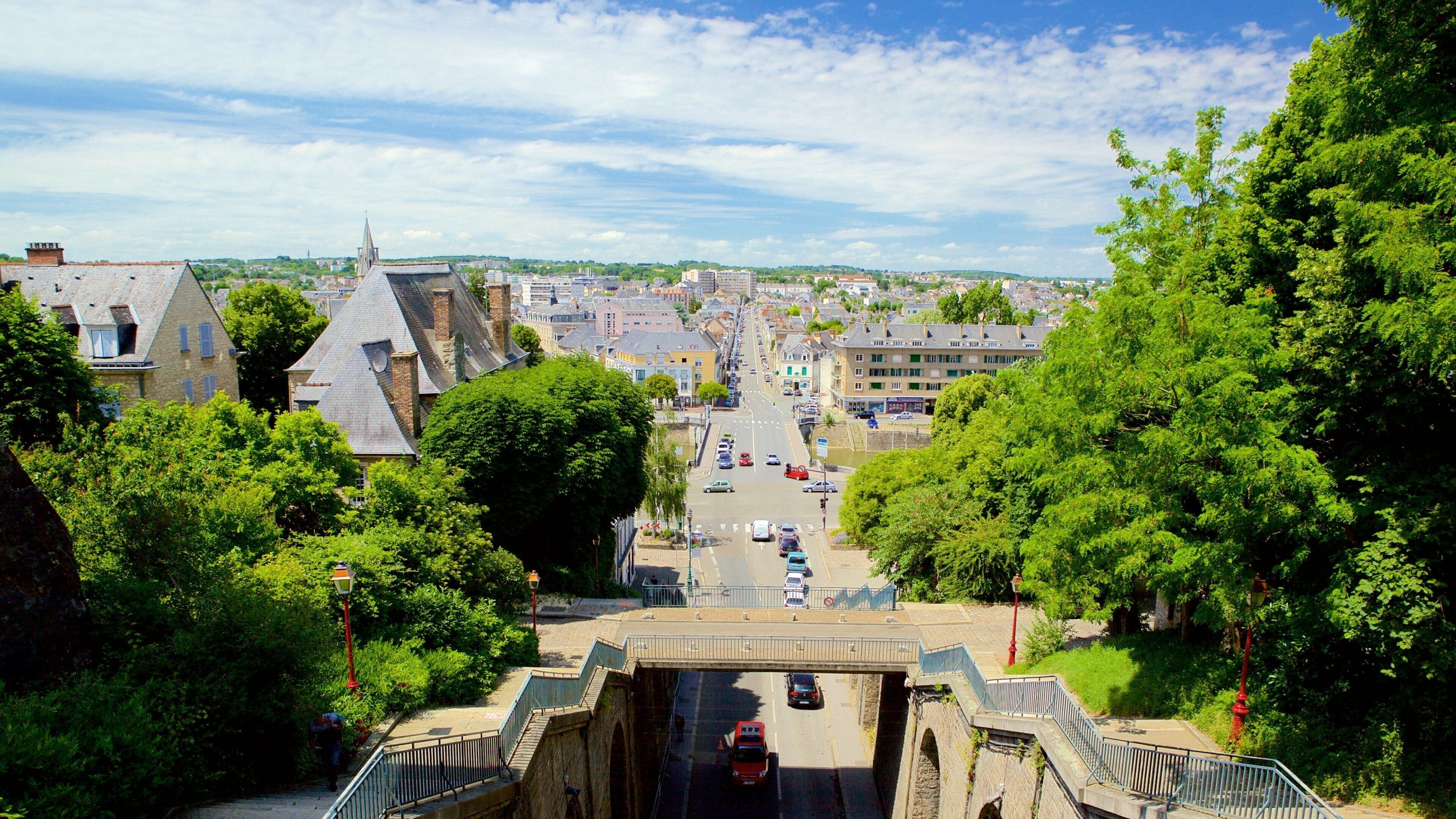 Een stad met een opvallende kerktoren, een brug en weelderige begroeiing.