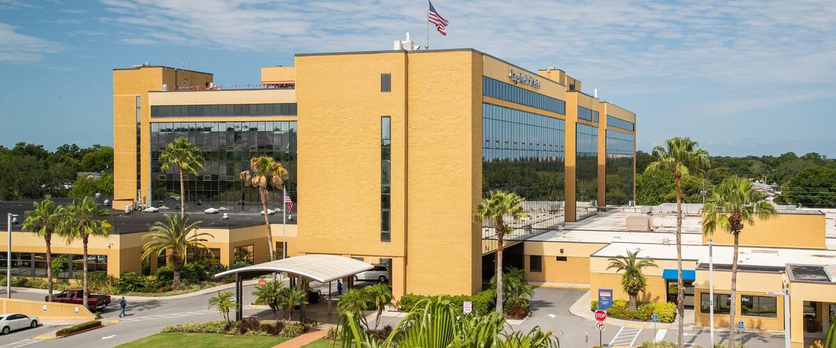 A large medical center with a yellow building, palm trees, and a parking lot.