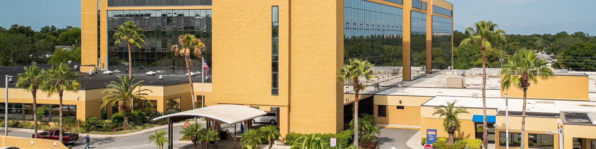 A large medical center with a yellow building, palm trees, and a parking lot.