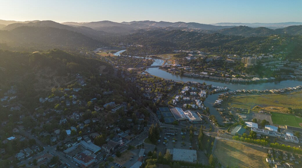 Arial wide of town with river running through, lots of blue water and green trees, golden hour sunset shining