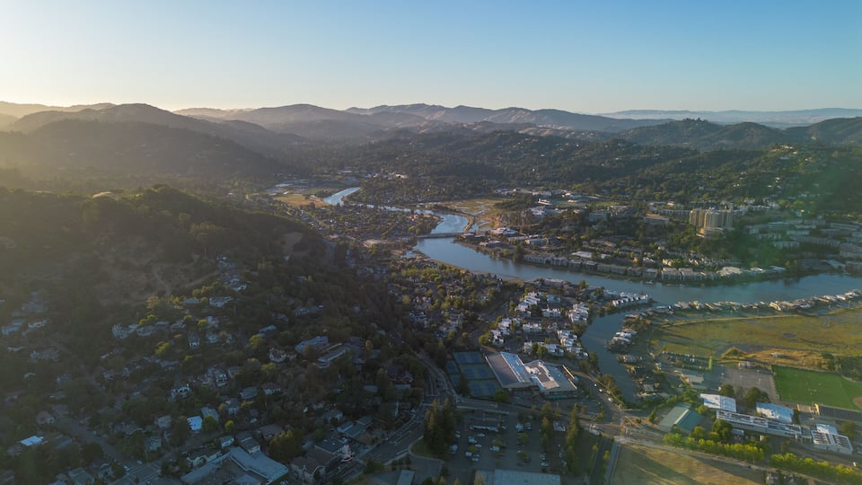 An aerial view of a town with a river, mountains, and residential areas.
