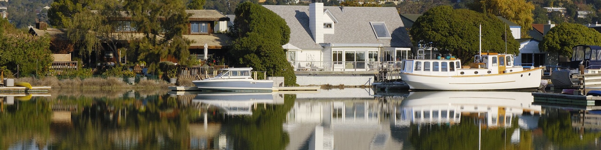 Nice houses with boats are reflected in calm waters of Corte Madera Creek in Larkspur,  California