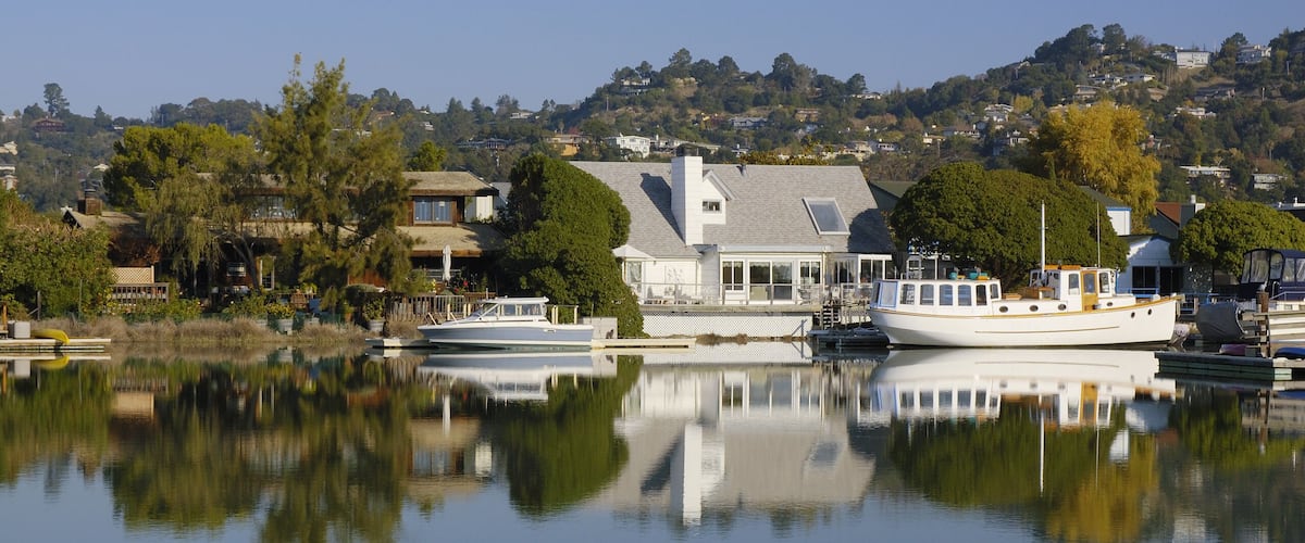 Nice houses with boats are reflected in calm waters of Corte Madera Creek in Larkspur, California