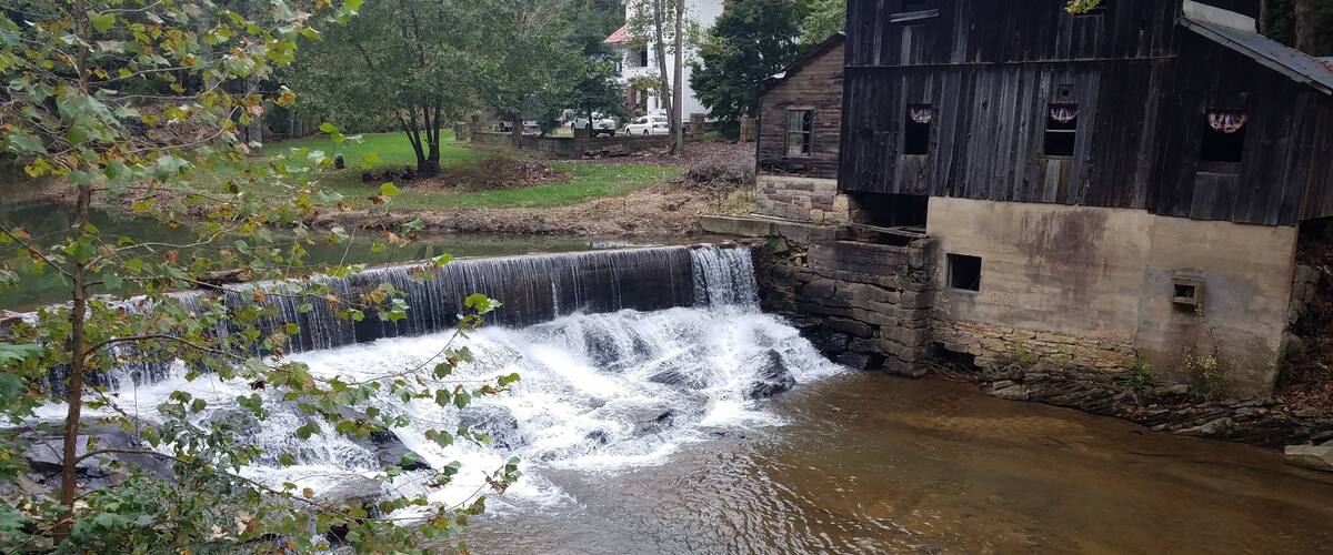 A waterfall, a wooden mill, and a stone building in a wooded area.