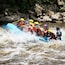Un grupo de personas en una balsa azul navegando por un río con rápidos, rodeado de rocas.