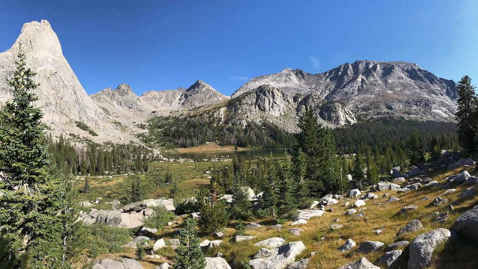 A mountainous landscape with a prominent rocky peak, a lake, and scattered trees.