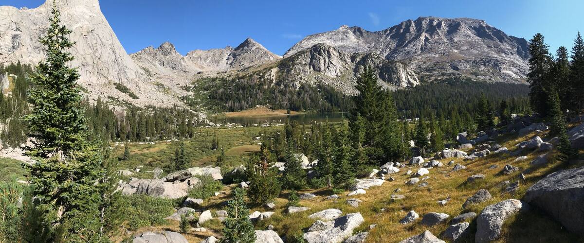 A mountainous landscape with a prominent rocky peak, a lake, and scattered trees.