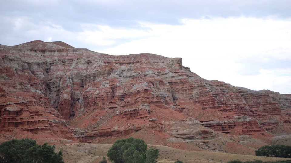 A layered red rock formation with a river in the foreground.