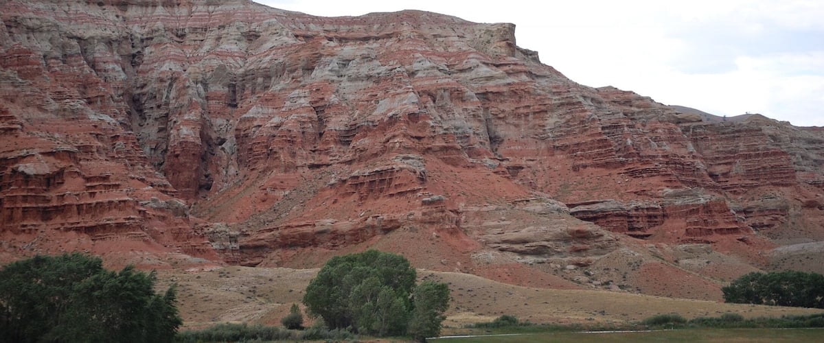 A layered red rock formation with a river in the foreground.