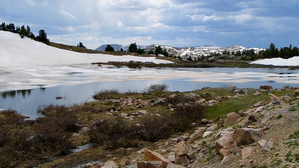 A mountainous landscape with a lake, snow-covered peaks, and scattered rocks.