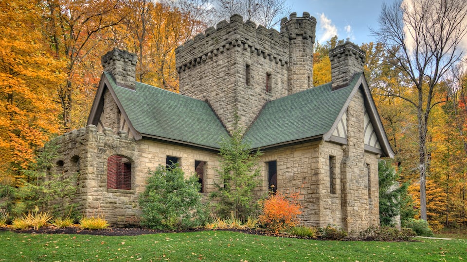 A stone castle with a green roof surrounded by autumn foliage.