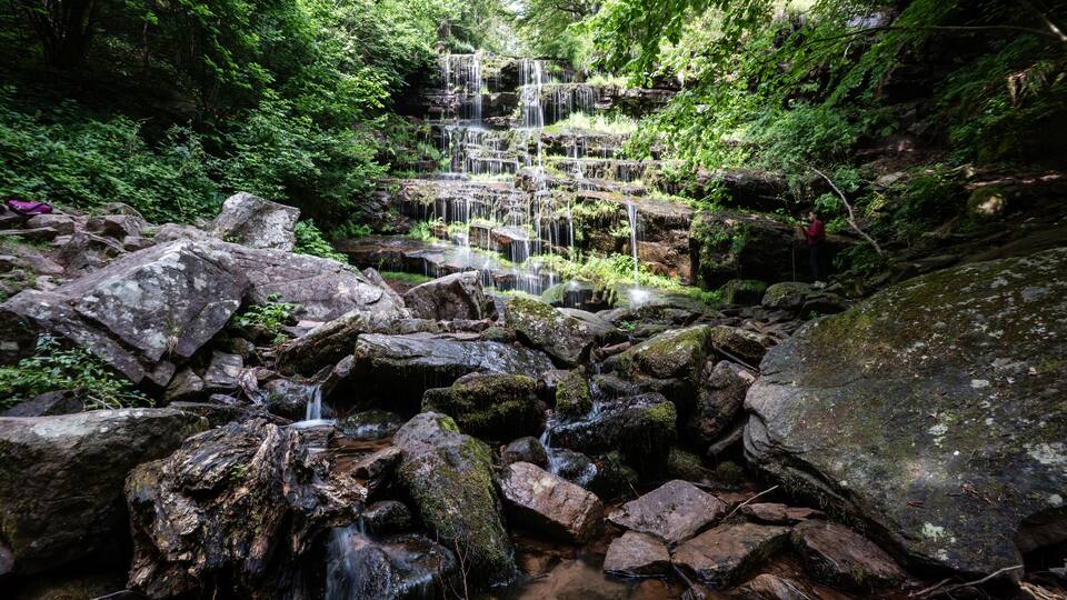 A multi-tiered waterfall surrounded by rocks and lush greenery.