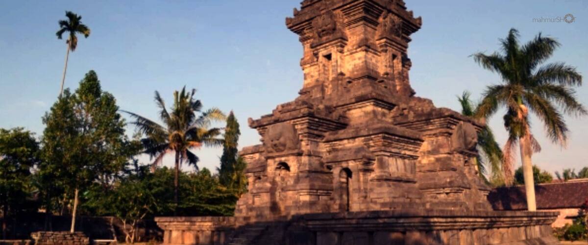 An ancient temple with intricate carvings and a tiered structure, surrounded by palm trees and greenery.