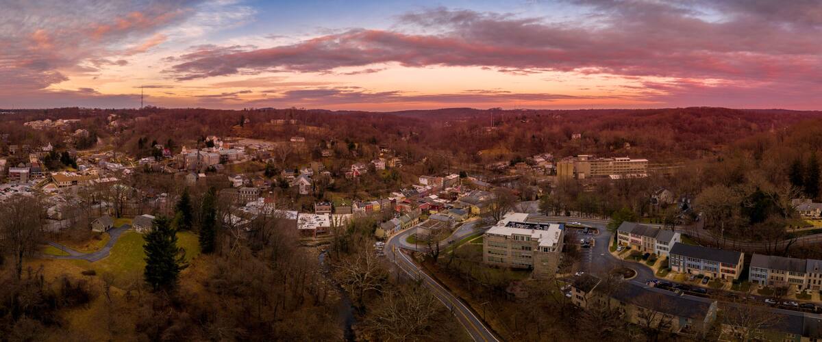 A town with a mix of residential and commercial buildings, surrounded by wooded areas, during sunset.
