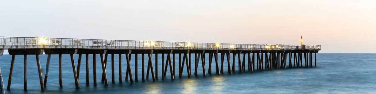 A pier extending into calm waters with a sandy beach in the foreground.