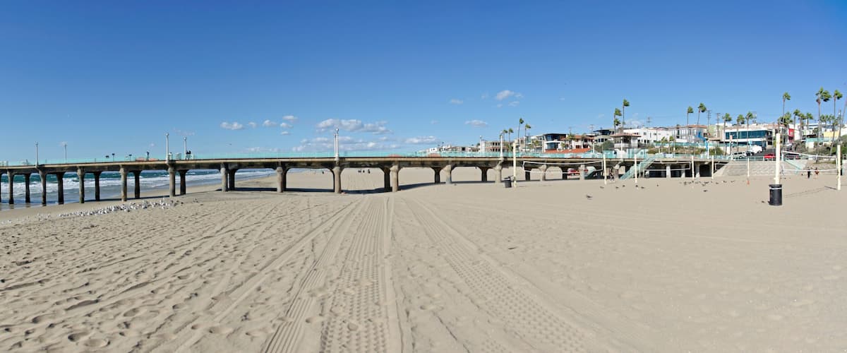 A beach with a pier extending into the ocean, a lighthouse, and a row of buildings along the shore.