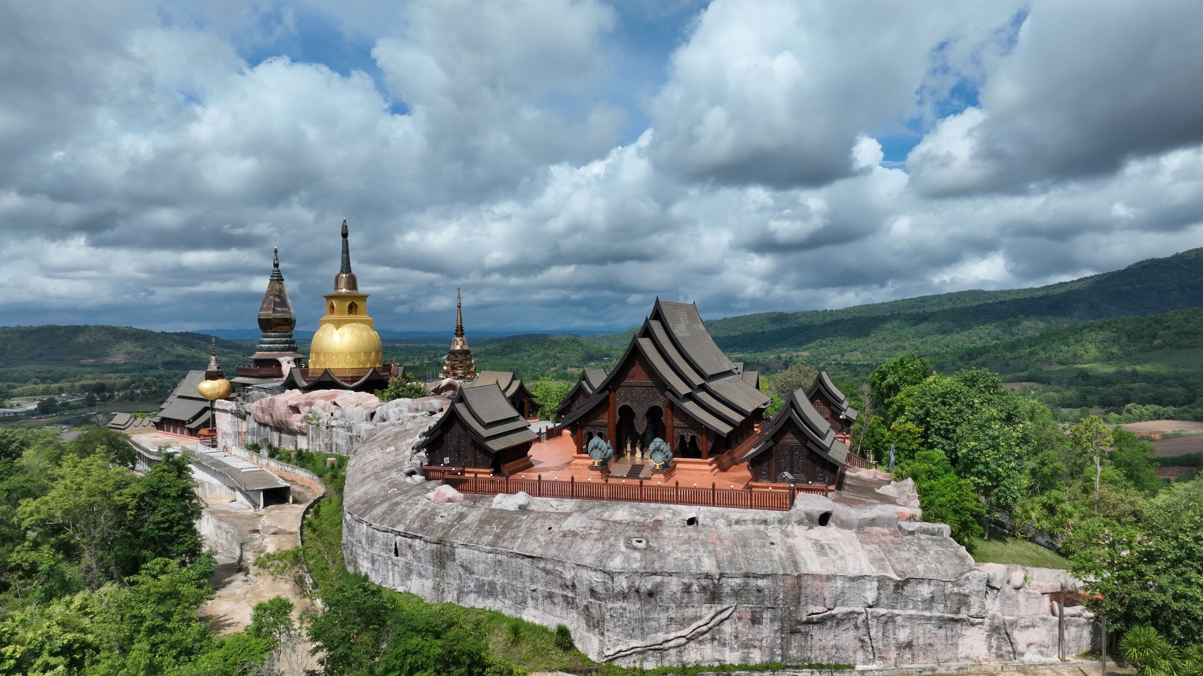 A temple complex with golden domes and traditional architecture, surrounded by lush green hills.