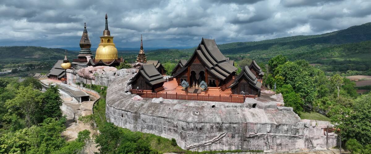 A temple complex with golden domes and traditional architecture, surrounded by lush green hills.