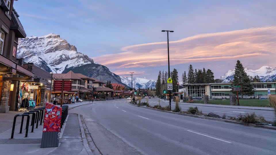 Street view of Banff Avenue in autumn evening. Snow capped Cascade Mountain with pink rosy sky in the background. Alberta, Canada.
