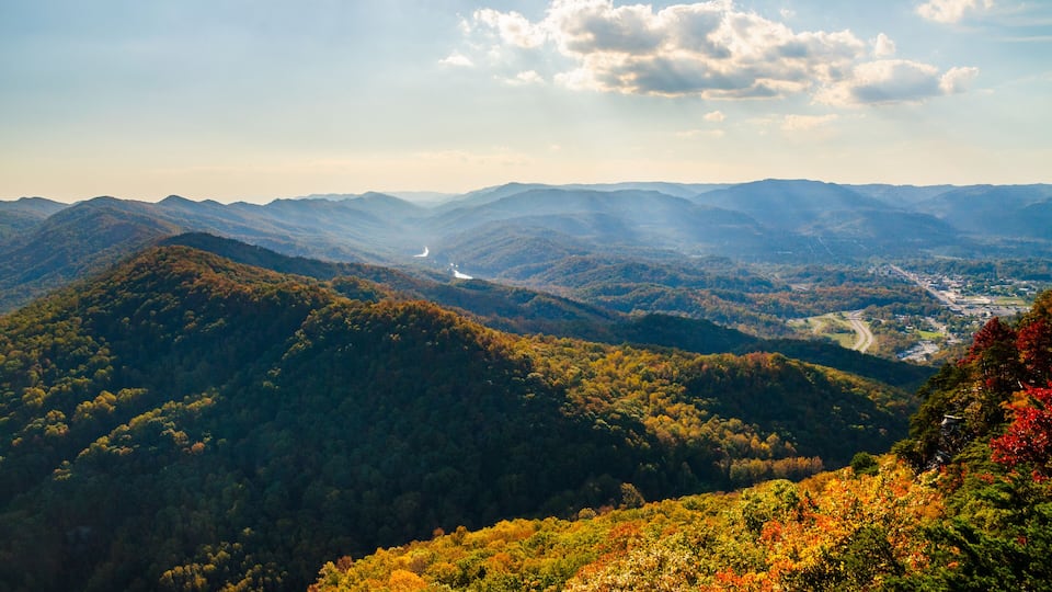 A mountainous landscape with a river, dense forests, and a distant town.