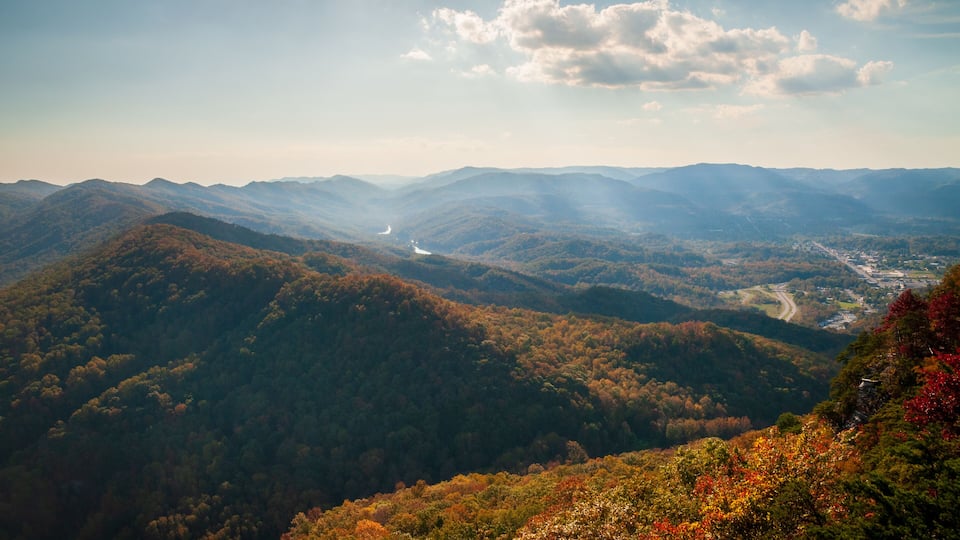A mountainous landscape with autumn foliage, a winding road, and a distant lake.