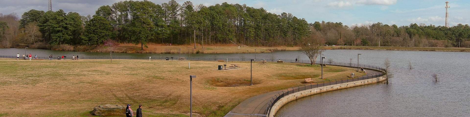 aerial shot of a gorgeous winter landscape at Rhodes Jordan park with a lake, yellow grass, lush green trees people walking with blue sky and clouds in Lawrenceville Georgia USA