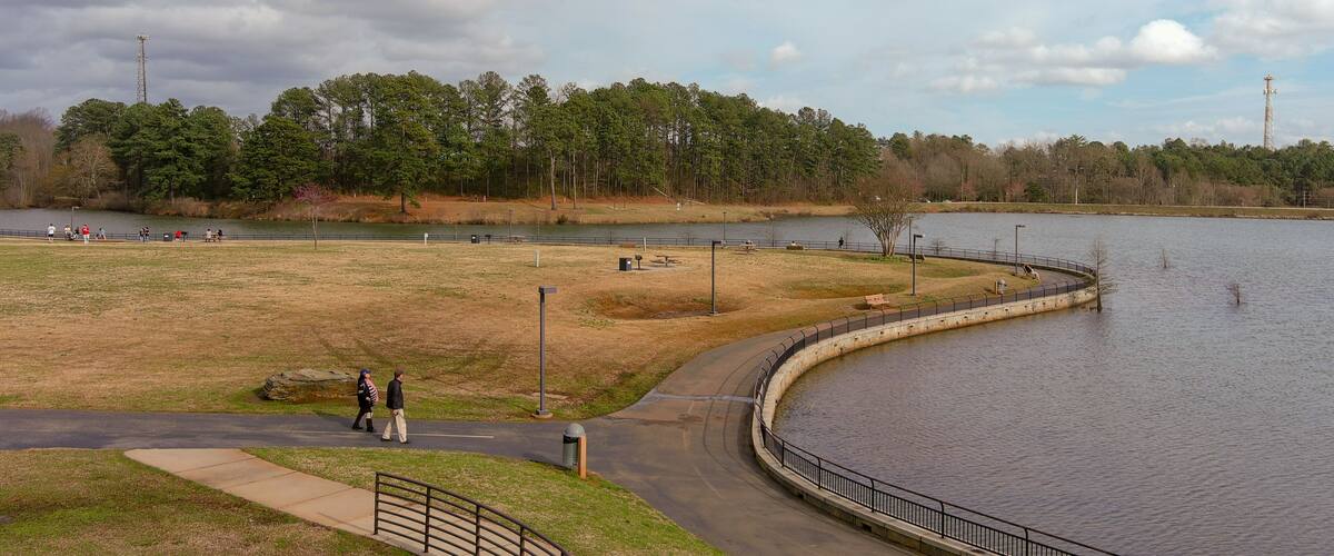 A lakeside park with walking paths, benches, and picnic areas.