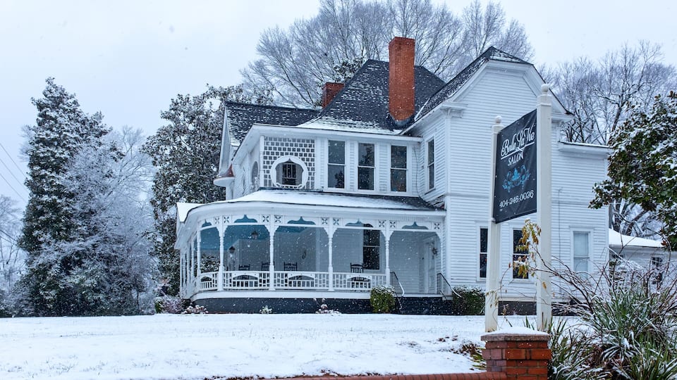 A white Victorian-style house with a porch and a sign for "Bella La La Salon" in front.