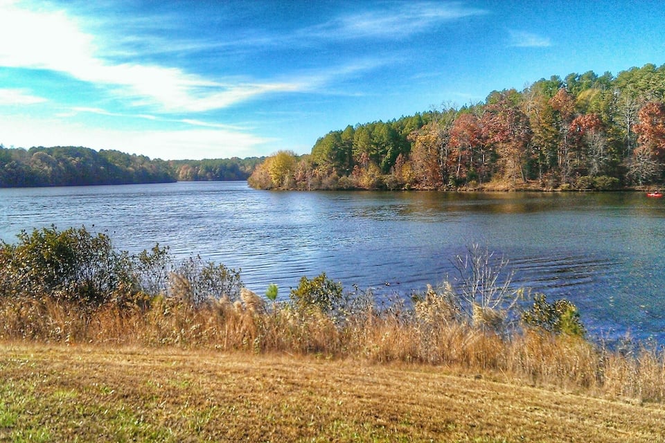 A calm lake surrounded by autumn-colored trees and grassy banks.