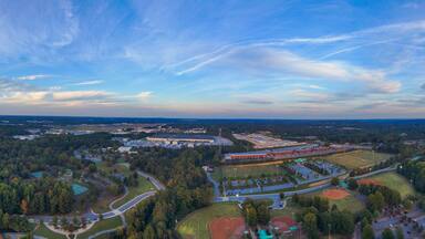 a stunning panoramic aerial shot of vast miles of lush green and autumn colored trees, still blue lake waters and blue sky with powerful cloud formations at Rhodes Jordan Park At Lawrenceville Lake in