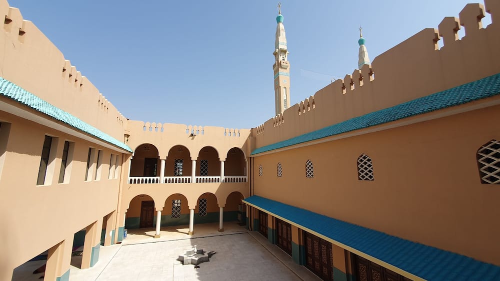 A courtyard with arches, a minaret, and a mosque with a blue-tiled roof.