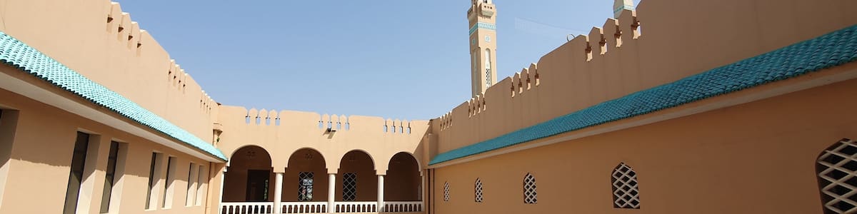 A courtyard with arches, a minaret, and a mosque with a blue-tiled roof.