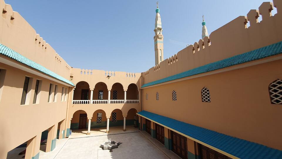 A courtyard with arches, a minaret, and a mosque with a blue-tiled roof.