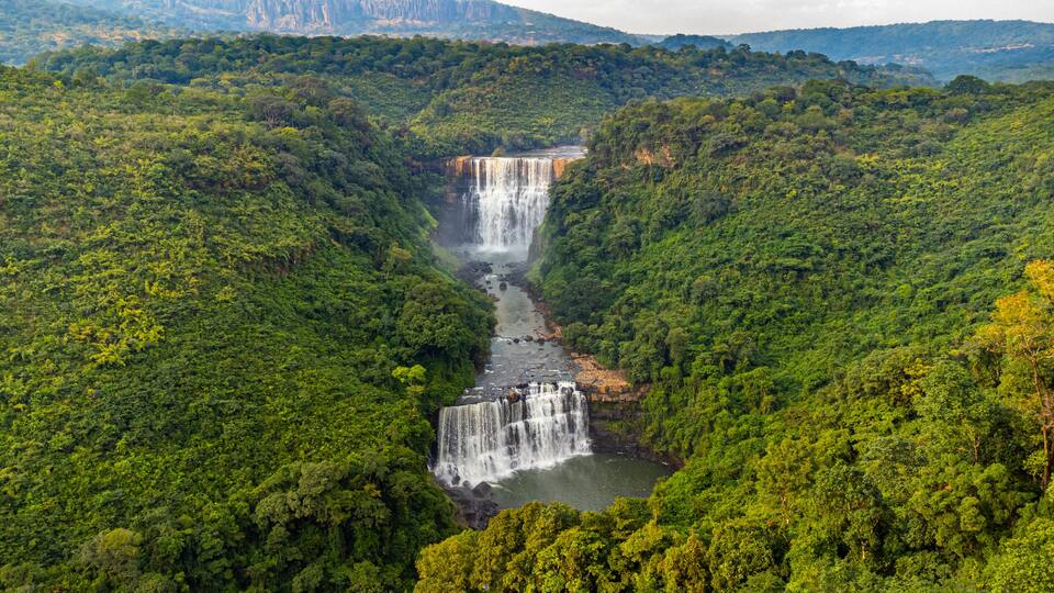 A waterfall cascading through a lush green valley surrounded by dense forest.
