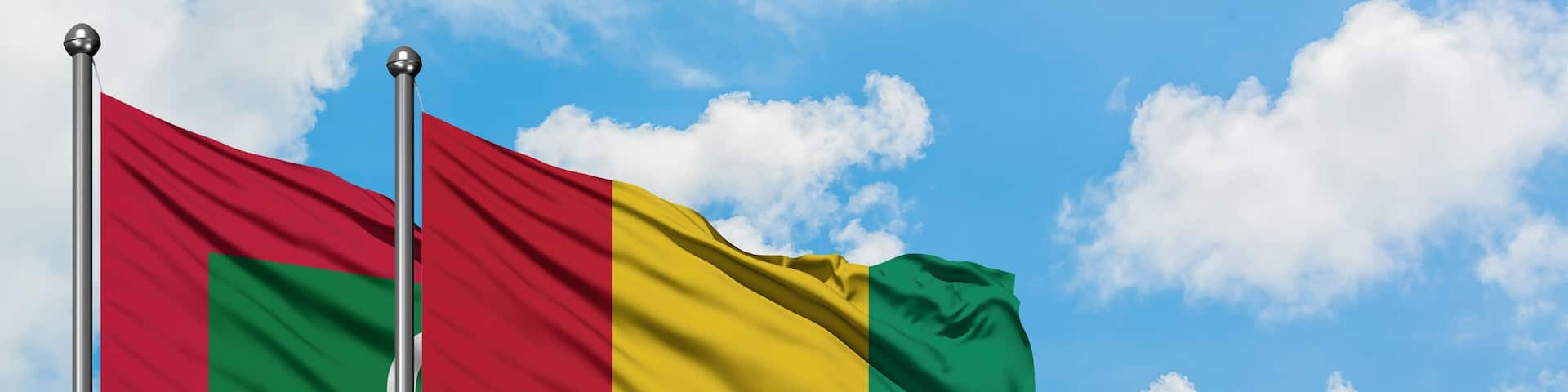 Maldives and Guinea flag waving in the wind against white cloudy blue sky together. Diplomacy concept, international relations.