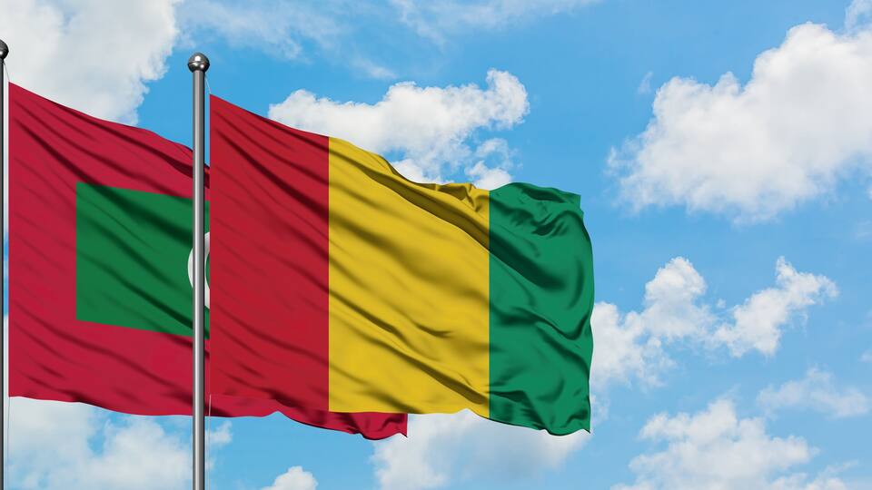 Two flags waving against a blue sky with clouds.