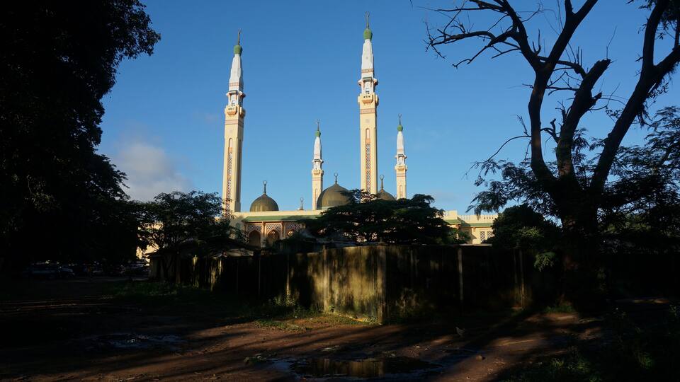 A mosque with four minarets and a dome, surrounded by trees and a dirt path.
