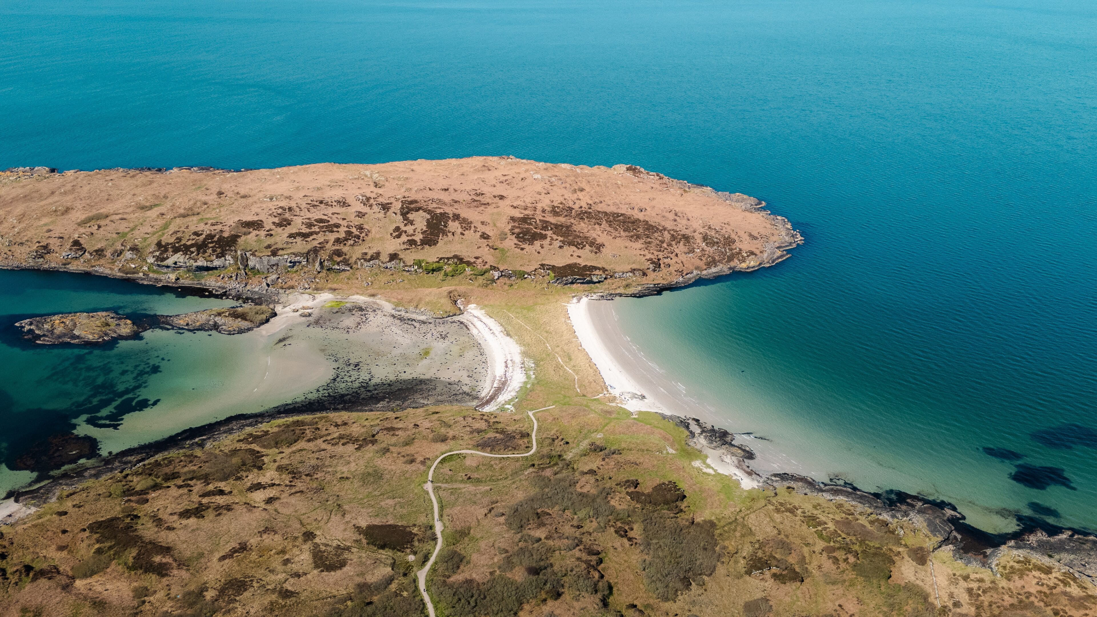 Aerial view of the Twin Beach with turquoise waters meeting the rugged shores, Isle of Gigha, Argyll and Bute, Scotland.