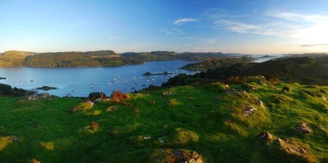 A coastal landscape with a body of water, green hills, and scattered rocks.