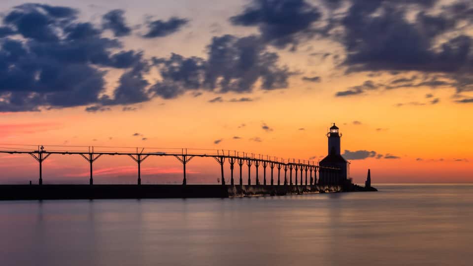A pier extending into the water with a lighthouse at the end, under a sunset sky.