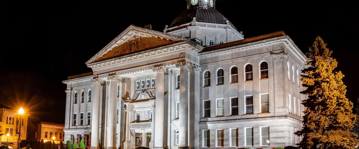 A large, illuminated government building with a clock tower and flag at night.