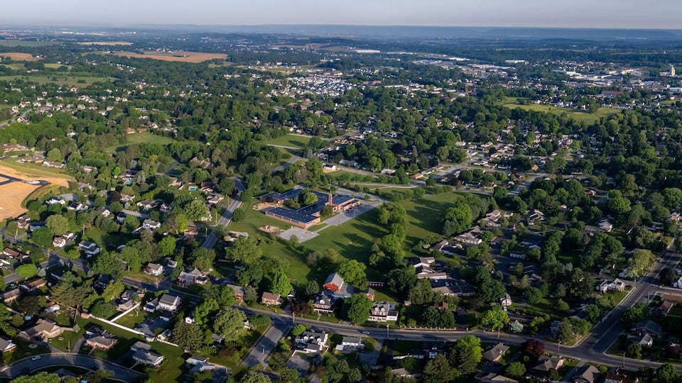 An aerial view of a suburban area with residential houses, green spaces, and a large open field.