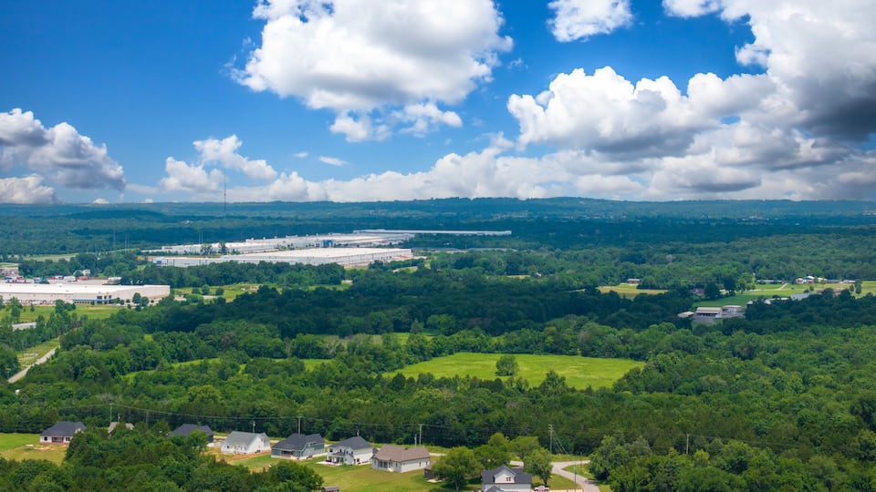 A large industrial area with a factory and warehouses surrounded by lush green fields and trees.